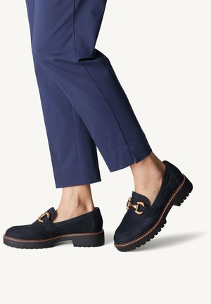 Mørkeblå ruskinds loafers med guldfarvet hardware, en kraftig platformsål og en struktureret overflade, parret med skræddersyede mørkeblå bukser.