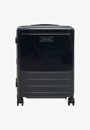 Valigia rigida nera con scanalature orizzontali, maniglia superiore, due maniglie laterali e quattro ruote. Presenta un logo del marchio sul fronte.