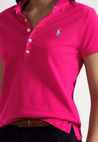 Πόλο πουκάμισο φούξια με γιακά, λευκά κουμπιά και τιρκουάζ λογότυπο. Φορεμένο με πλεγτή καφέ ζώνη πάνω από σκούρο παντελόνι.