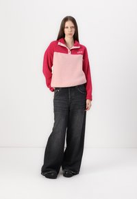 Fleece pullover in een gradient roze met een kraag en het GAP-logo. Gecombineerd met zwarte jeans met wijde pijpen. Zachte textuur, casual ontwerp.