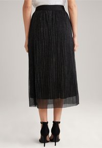 Černá plisovaná midi sukně s přiléhavým pasem, vyrobená z lehké látky s kovovými nitěmi. Nošena s černými vysokými podpatky.