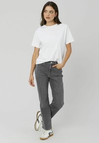 T-shirt en coton blanc, coupe ample, associé à un jean en denim gris foncé. Les baskets présentent une base blanche avec des accents noirs et des semelles en gomme.
