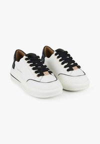 Weiße Turnschuhe mit schwarzen Schnürsenkeln und Akzenten, mit einer strukturierten Rückseite, goldfarbenen Beschlägen und einer dicken, strukturierten Sohle.