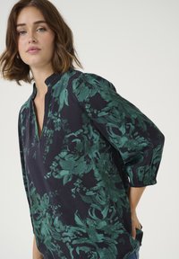 Blouse marine avec imprimé floral vert, tissu léger, décolleté en v, manches bouffantes trois-quarts et poignets élastiques.