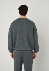Sweatshirt gris avec un tricot texturé, épaules tombantes et poignets côtelés, associé à un pantalon assorti en coupe décontractée.