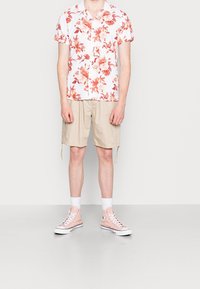 Camicetta bianca a maniche corte con fiori rosa e arancioni, abbinata a pantaloni cargo beige e sneakers alta rosa.
