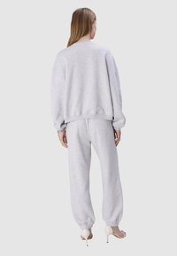 Grauer Sweater mit überschnittenen Schultern und gerippten Bündchen, kombiniert mit passenden grauen Trainingshosen mit elastischen Säumen. Das Model trägt High Heels.