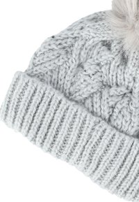 Vaaleanharmaa neulottu hattu, jossa on kaapeli- ja ribbikuvioida, ja jonka päällä on pehmeä pom-pom. Pehmeä, teksturoitu lanka tarjoaa lämpöä.