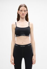 Zwarte bralette met dunne bandjes en een Calvin Klein logo band. Gecombineerd met zwarte high-waisted leggings met een vergelijkbare logo tailleband.