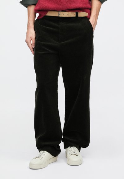 Sötétzöld kordbársony nadrág, egyenes szabással és finom textúrával, világosbarna övvel és fehér sportcipővel viselve.