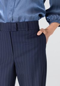 Marineblauwe gestreepte broek gemaakt van een gladde stof, met een platte tailleband, zijzakken en een getailleerde pasvorm.