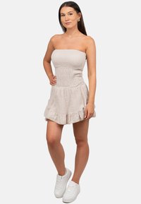 Smock jurk in lichtbeige, strapless met gestructureerde stof, gerimpelde zoom en een aansluitend lijfje. Gekoesterd met witte sneakers.