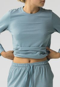 Jasnoniebieska koszula z długim rękawem wykonana z miękkiej bawełny, połączona z jasnoniebieskimi spodniami piżamowymi z małym wzorem w kokardki i elastycznym pasem.