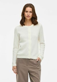 Cardigan blanco de punto con un patrón texturizado, cuello redondo y puños acanalados. Presenta un cierre de botones en el frente y un diseño ajustado.