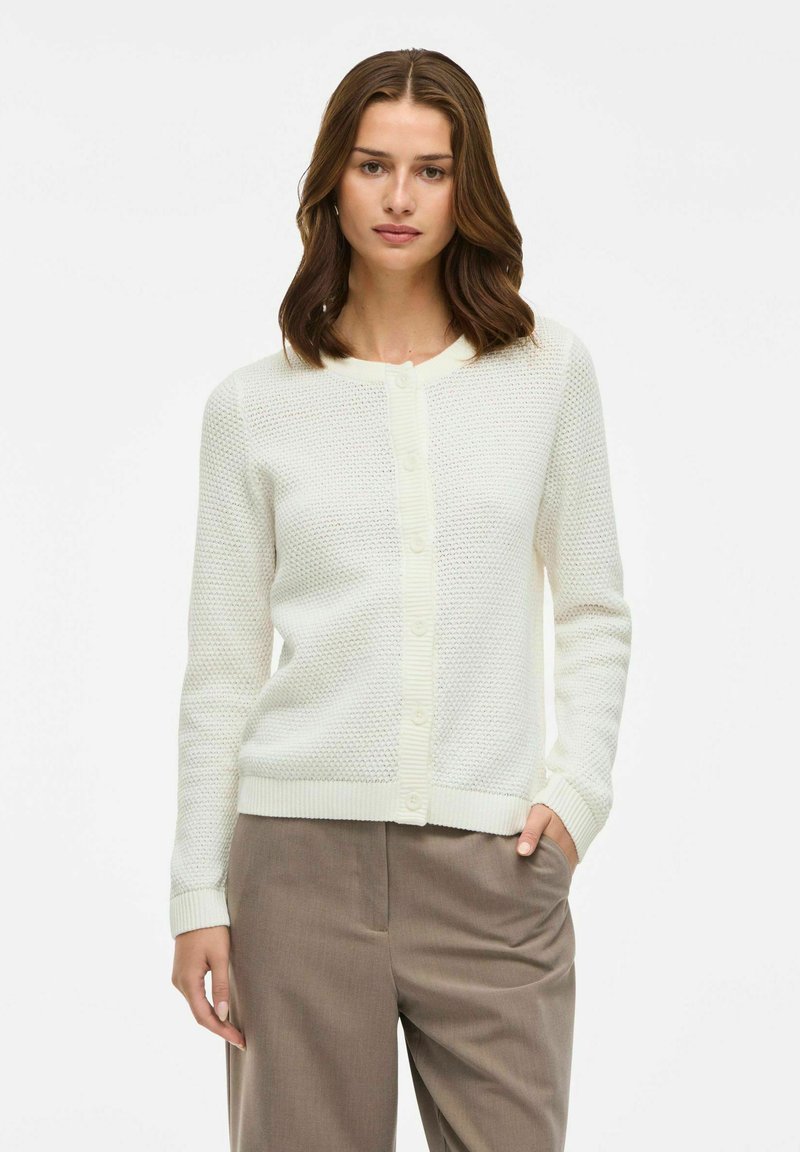 Cardigan blanco de punto con un patrón texturizado, cuello redondo y puños acanalados. Presenta un cierre de botones en el frente y un diseño ajustado.