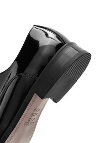 Błyszczący czarny skórzany obcas buta wizytowego z warstwową podeszwą i widocznym przeszyciem na gładkiej cholewce.