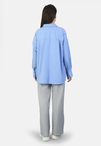 Camisa de botones de largo azul claro con cuello, diseñada con un corte relajado. Combinada con pantalones grises de corte holgado y zapatillas blancas.