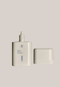 Base Natural Radiance de Korres en un bote rectangular con un nozzle cónico, de color crema y tapa texturizada blanca.