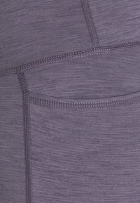 Fioletowe legginsy sportowe wykonane z teksturowanej, elastycznej tkaniny, z boczną kieszenią i płaskimi szwami dla komfortu i trwałości.