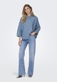 Prevelik svetlo moder jeans srajca z vzorcem srčkov, kombinirana s širokimi svetlo modrimi kavbojkami. Obe obleki imata sproščen dizajn in mehko teksturo.