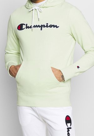 Felpa verde chiaro con tasca frontale, cordino bianco e logo "Champion" ricamato in nero e rosso. Presenta dettagli a costine sui polsini.