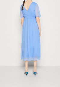 Robe en chiffon bleu avec un dos en V, des manches courtes et une taille élastique. L'ourlet tombe au milieu du mollet. Associée à des sandales à talons bleues.
