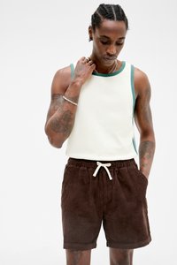 Kremet tank topp med teal stripet kant, parret med brune kordfløjl shorts med elastisk talje og snoretræk. Hudtone og tatoveringer synlige.