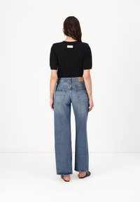 Mustapaitainen lyhythihainen paita, jossa on logotagi, yhdistettynä korkeavyötäröisiin, leveälahkeisiin sinisiin farkkuihin, joissa on takataskut ja strukturoitu pinta.