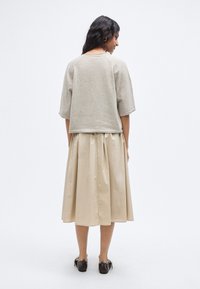 Haut à manches courtes en maille beige à coupe décontractée, associé à une jupe plissée fluide de couleur crème, et des chaussures foncées à finition brillante.