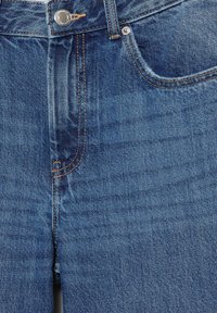 Plave traperice od trapera koje prikazuju džep sprijeda, dugme, petlju za remen i detaljno šivanje na teksturiranoj tkanini.