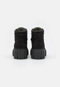 Botas de tobillo de ante negro con un diseño acolchado, que cuentan con una suela de goma negra gruesa y texturizada. Forradas con un material verde oscuro en la abertura.