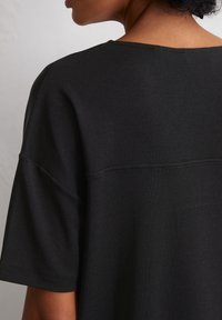 Black short-sleeve top, featuring a relaxed fit, crew neckline, and smooth texture. Visible stitching along the shoulder seam.