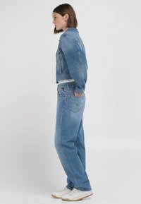 Ljusblå denimjacka med kort passform, i kombination med löst sittande ljusblå jeans och vita sneakers. Slät textur, minimala detaljer.