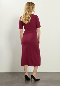 Mauve sukienka midi z gładkiego materiału, z krótkimi rękawami, dopasowanym wcięciem w talii i prostym krojem. Nosi z czarnymi szpilkami.
