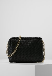 Sac à main tissé noir avec une surface texturée, doté d'une chaîne dorée et d'une forme rectangulaire. Fermeture simple en haut.