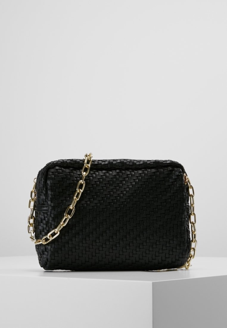 Sac à main tissé noir avec une surface texturée, doté d'une chaîne dorée et d'une forme rectangulaire. Fermeture simple en haut.