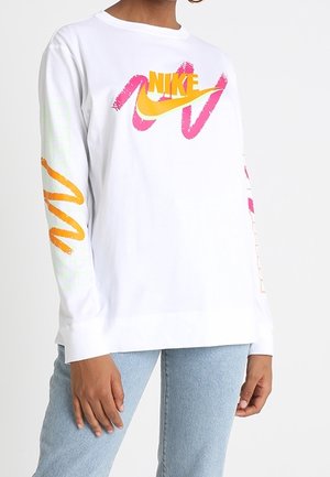 White long-sleeve shirt with yellow and pink Nike logo on chest and colorful brushstroke designs on sleeves, worn with light blue jeans.