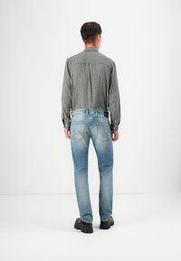 Camisa de cuadros para hombre en blanco y negro, combinada con jeans desgastados de color azul claro y botas negras gruesas, vista desde atrás.