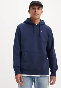 Donkerblauwe hoodie van katoen, met een kangoeroezak, een capuchon met trekkoord en een klein rood logo op de borst. Textuurstof.