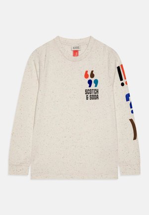 Chemise crème à manches longues avec des guillemets colorés et le texte "SCOTCH & SODA" sur le devant, et des signes de ponctuation en gras sur la manche droite.