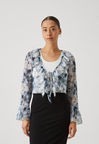 Avskuren, genomskinlig blus med blommönster i blått och vitt, volangkrage, knytning och trumpetsärmar. Stylad över en ribbad topp.