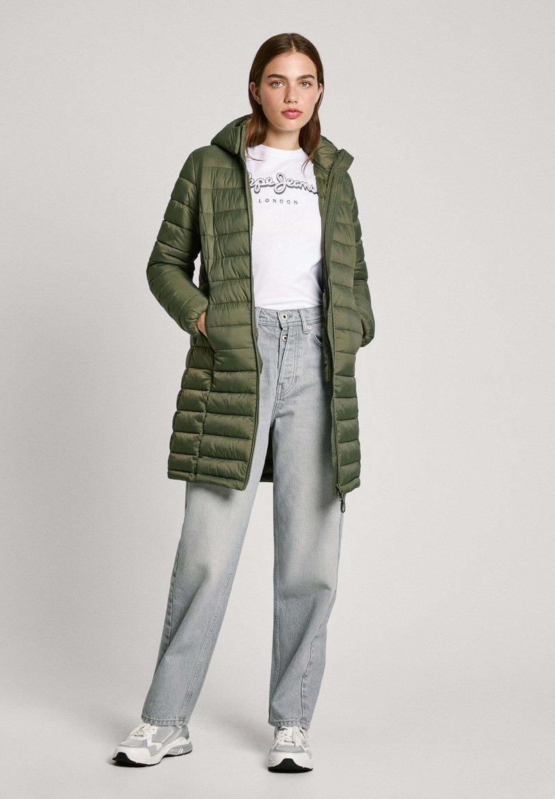 Abrigo acolchado verde oliva con capucha, cierre de cremallera en la parte delantera y dos bolsillos laterales. Combinado con una camiseta blanca con logo y jeans de cintura alta en azul claro.