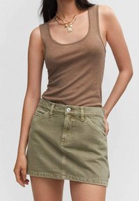 Bruine mouwloze tanktop gecombineerd met een groene denim minirok. De rok heeft zijzakken en een metalen knoopsluiting.