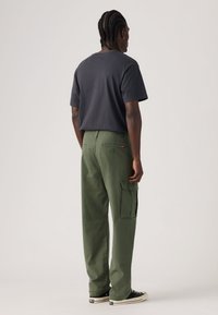 Μαύρο βαμβακερό t-shirt και πράσινο παντελόνι cargo με πλαϊνές τσέπες και πίσω τσέπη. Φορεμένα με μαύρα αθλητικά παπούτσια που έχουν λευκές λεπτομέρειες.