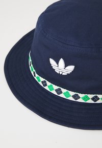 Navy blue bucket hat made of woven fabric, featuring a white embroidered logo and a decorative green and black checkered band.