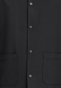 Black button-up jacket featuring a smooth texture, two front pockets, and black snap closures. Simple and modern design.