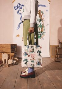 Fényes anyagból készült virágmintás bevásárlótáska, zöld fogantyúkkal és színes állatmintákkal.