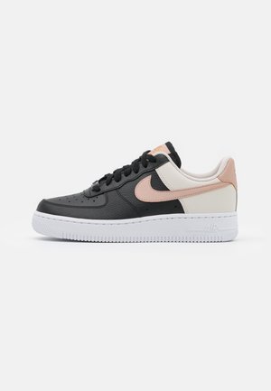 Niskie tenisówki z czarnej i kremowej skóry z jasnoróżowym logo Nike i białą podeszwą, pokazane od zewnętrznej strony.