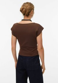 T-shirt en coton marron à manches courtes et col large, associé à un pantalon en denim bleu foncé avec deux poches arrière.