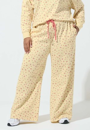 Persona che indossa pantaloni pigiama gialli floreali larghi con coulisse rosa e top abbinato, abbinati a sneaker bianche.